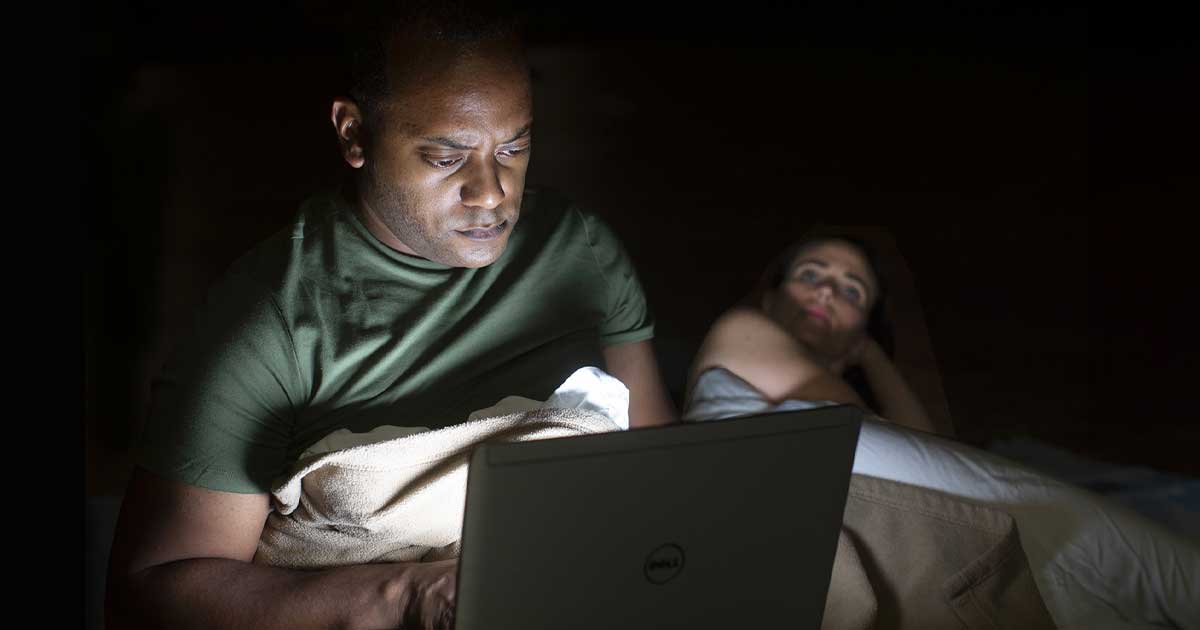 Actor looks at computer in bed